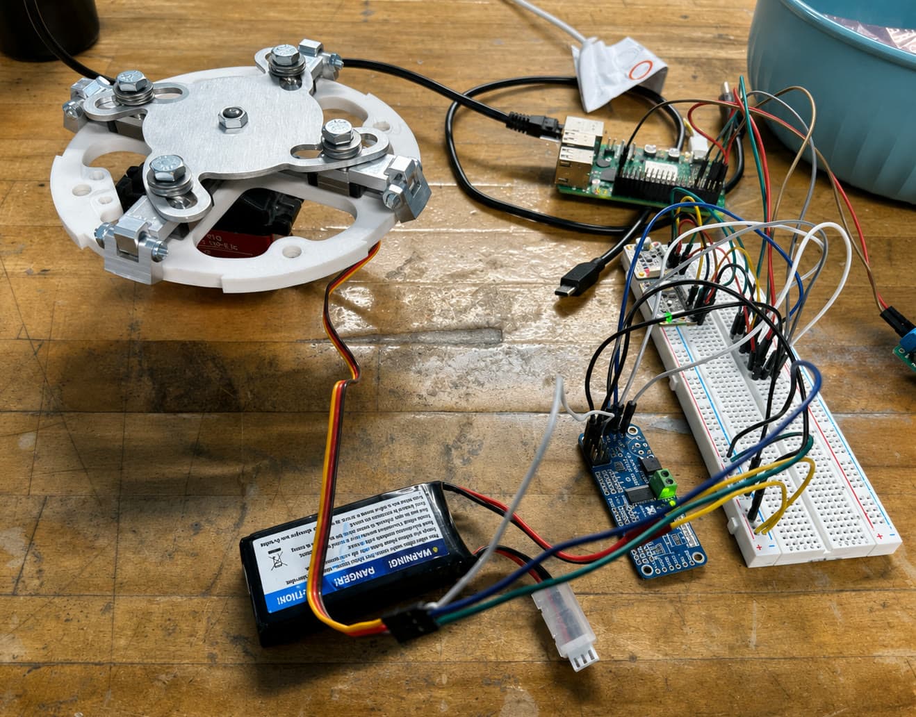 Bench test setup with the airbrakes mechanism wired to a single-board computer, breadboard, and battery on a workbench
